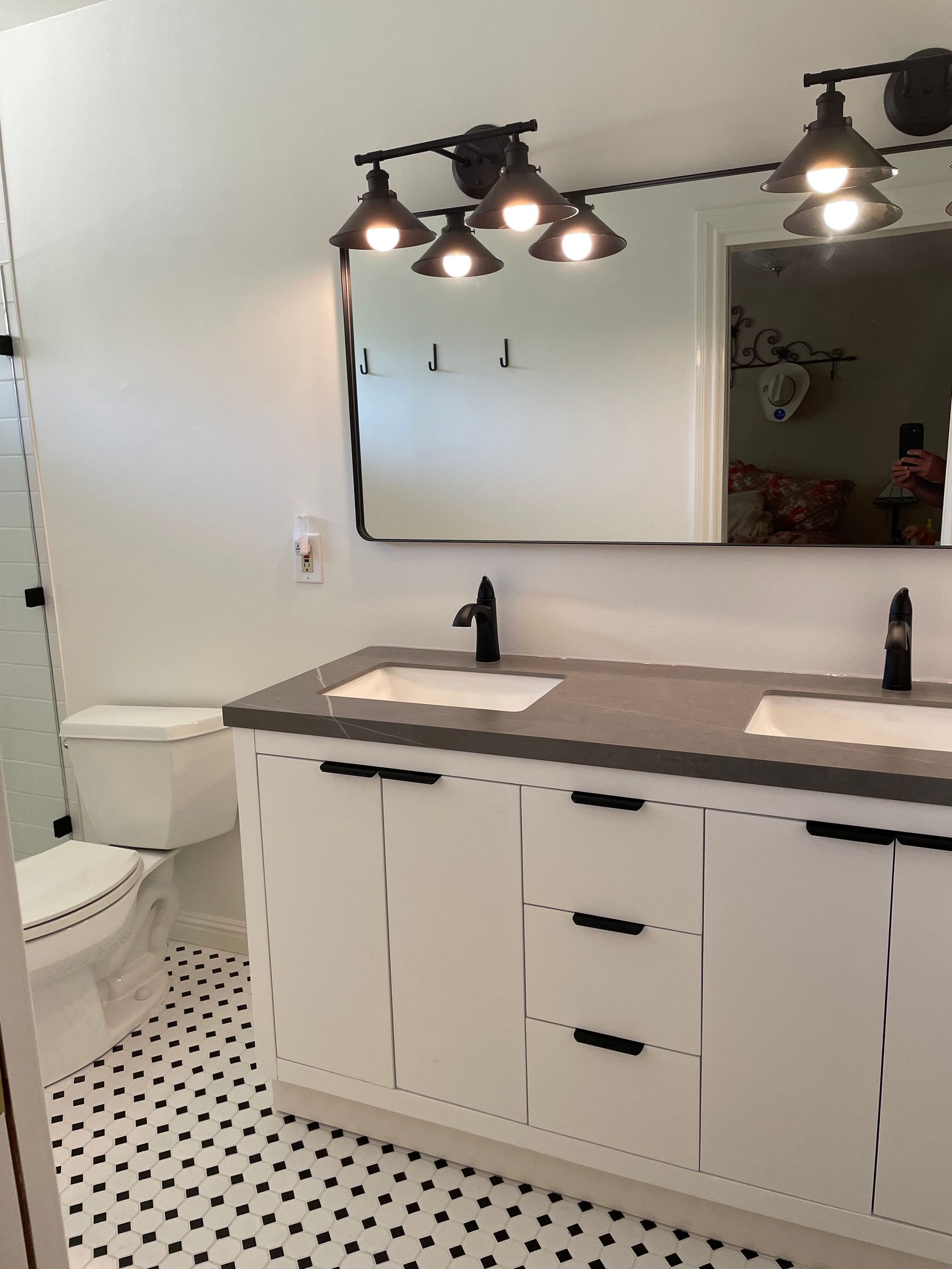 A modern bathroom with a double vanity, dark gray countertops, white cabinets, black hardware, and black and white tile.