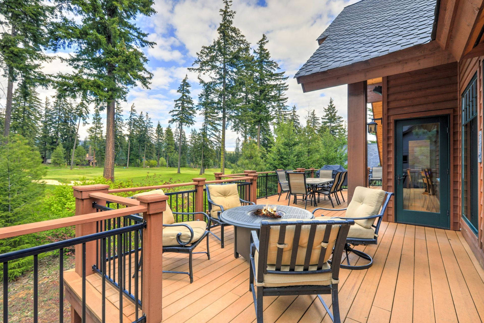 Wooden deck with outdoor furniture overlooking a green golf course, surrounded by trees.