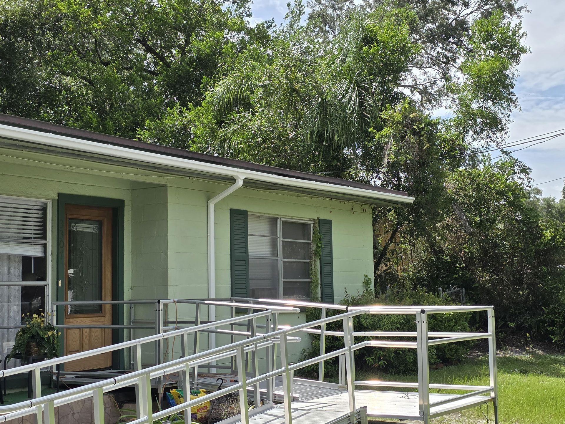A light green house with a wheelchair ramp, surrounded by trees.