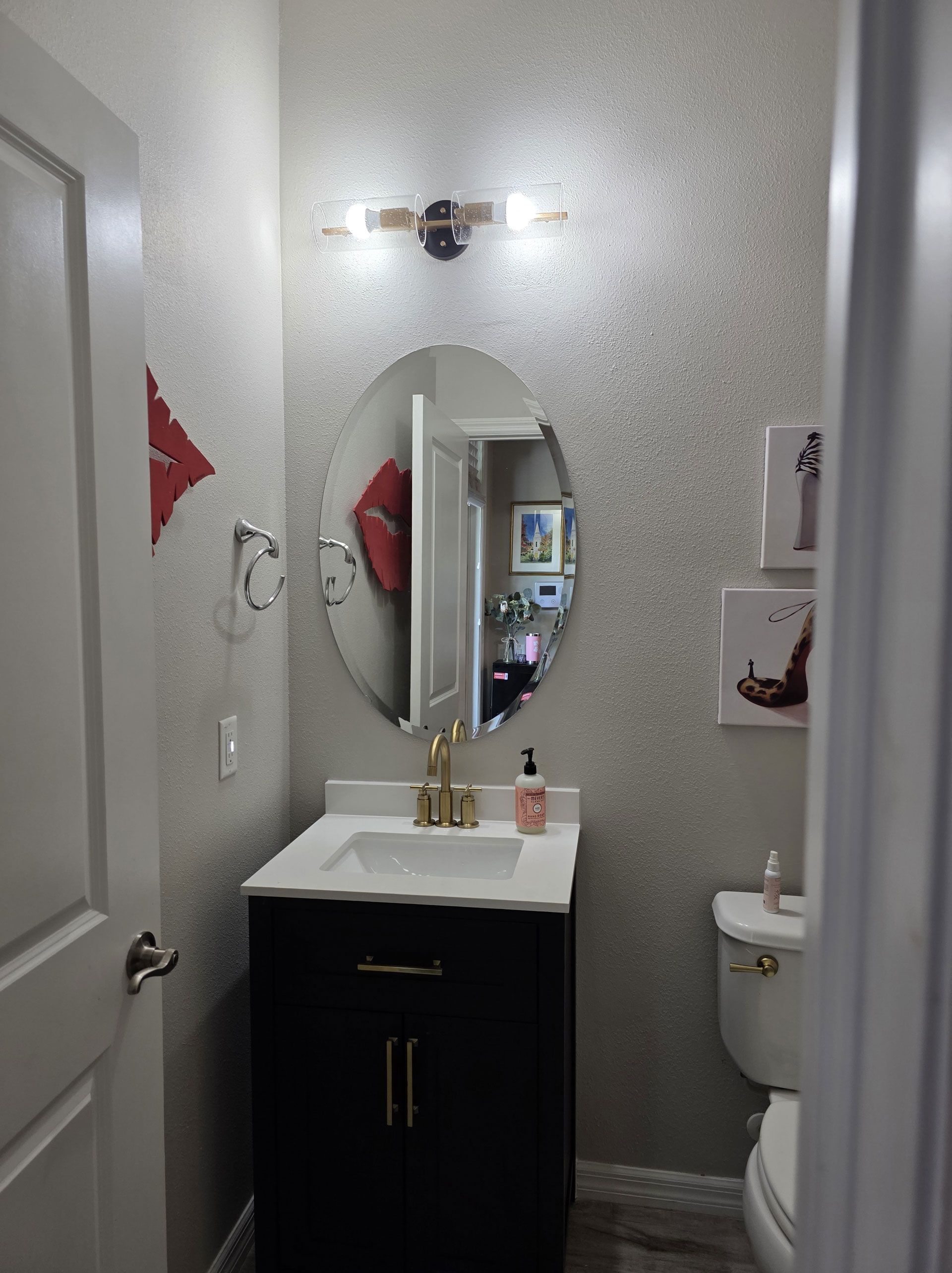 Powder room with sparkly silver textured walls, black vanity, oval mirror, and artwork.