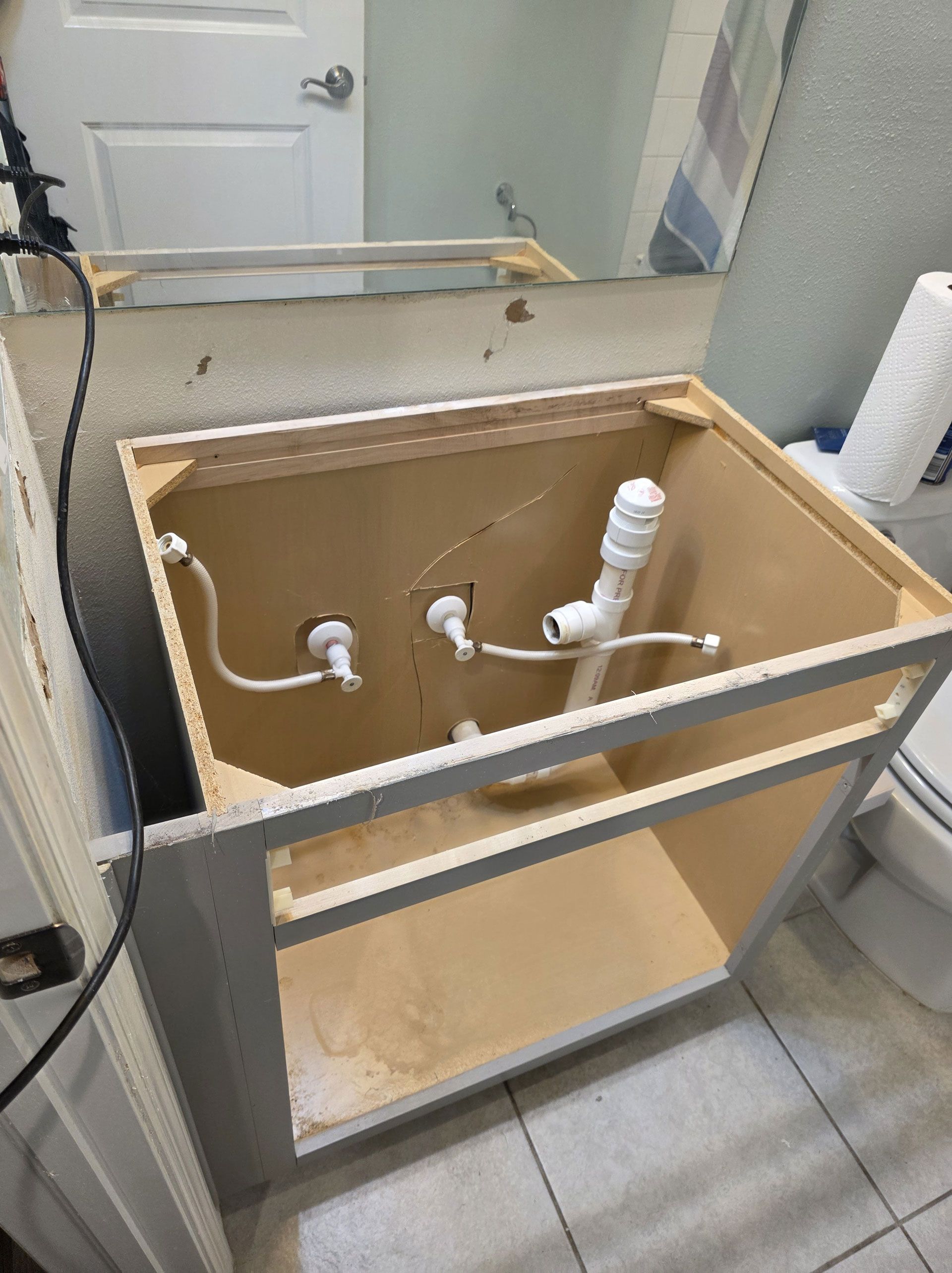 Open bathroom vanity cabinet with exposed plumbing, awaiting sink installation.