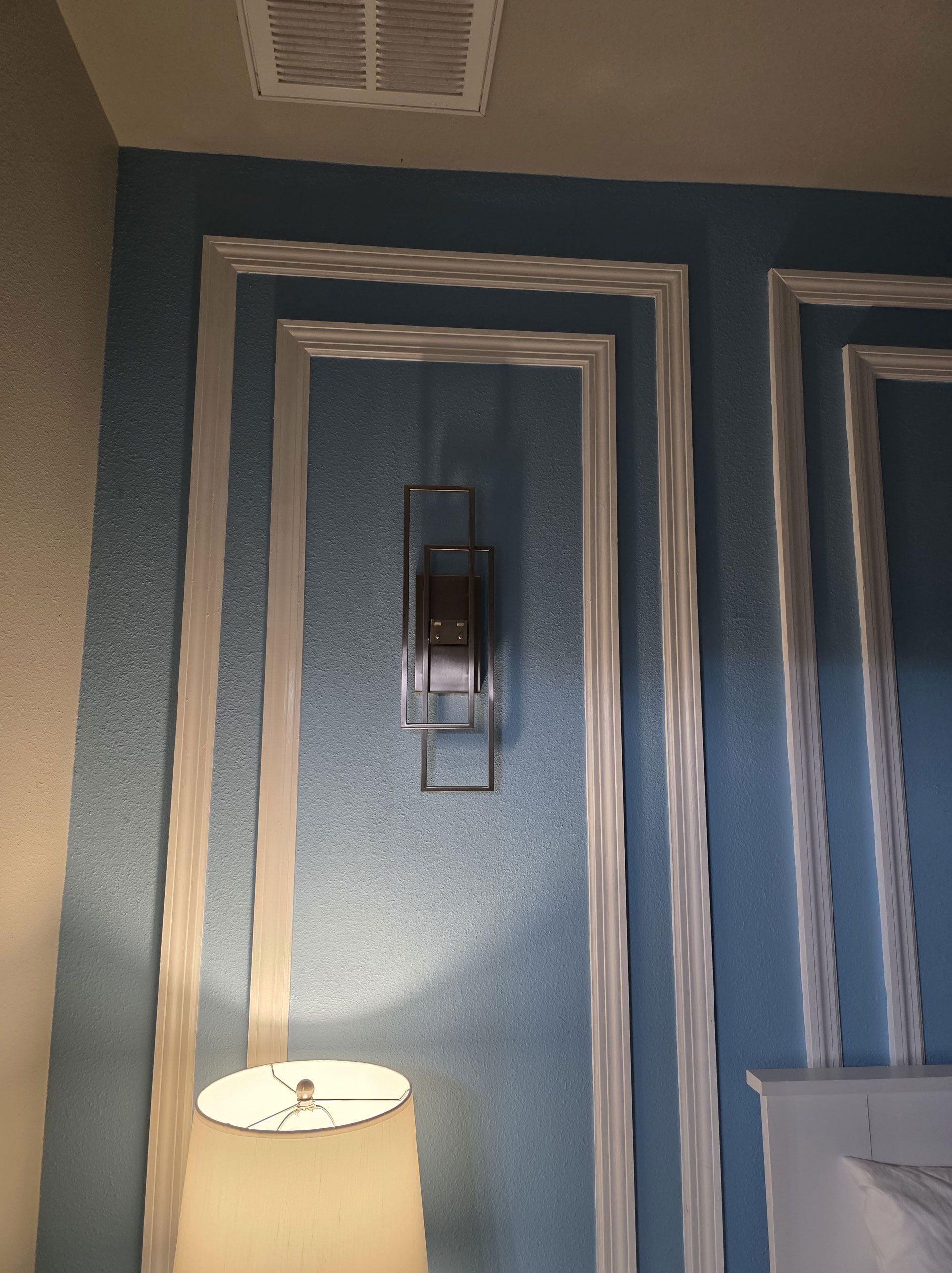 Blue wall with white trim and a geometric light fixture. A lampshade is visible at the bottom.