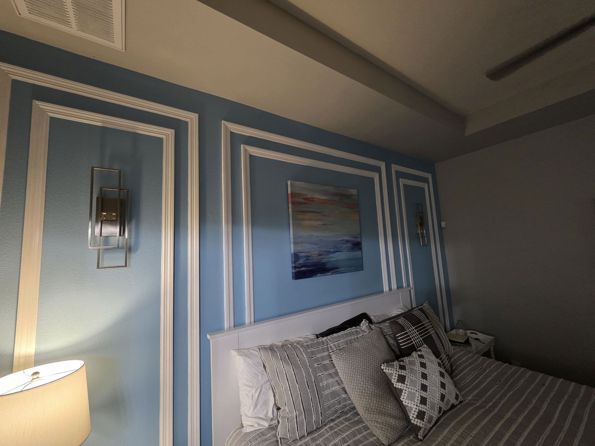 Bedroom with blue walls, decorative molding, bed, artwork, and lamps.