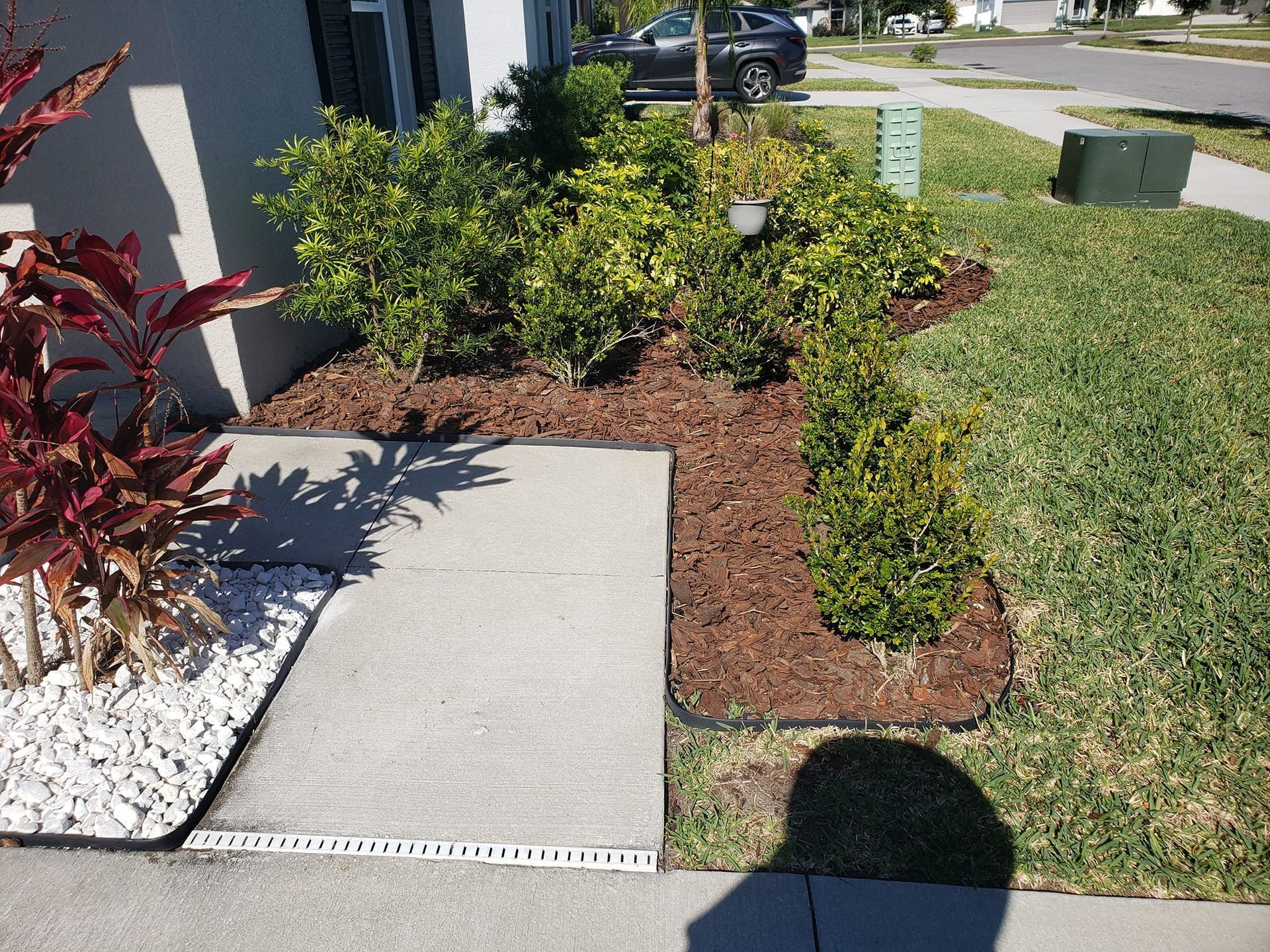 A shadow of a person is cast on a sidewalk in front of a house.