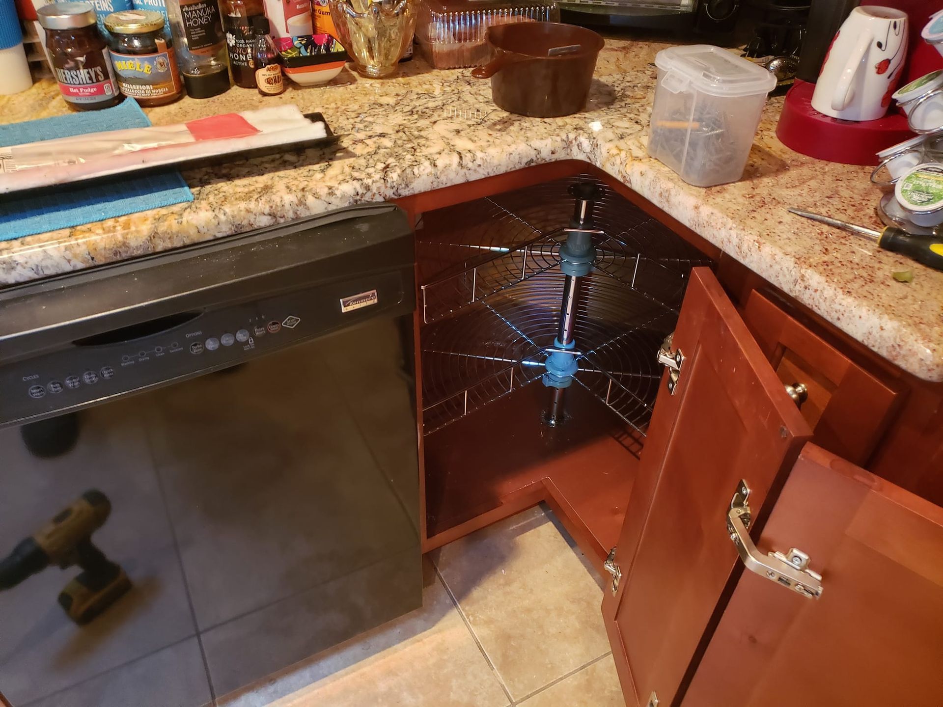 A kitchen with a black dishwasher , wooden cabinets , granite counter tops and a spice rack.