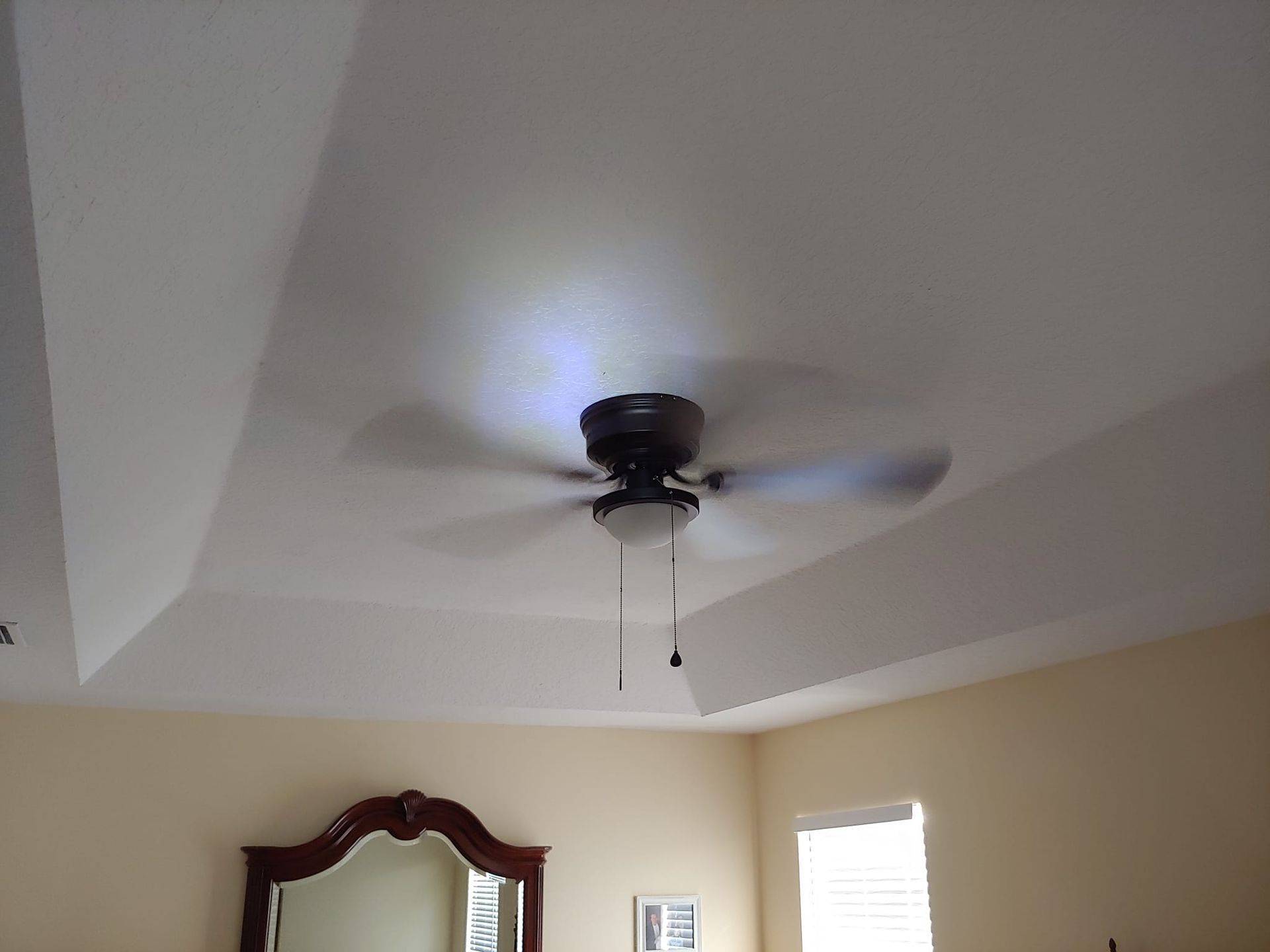 A bedroom with a ceiling fan and a mirror.