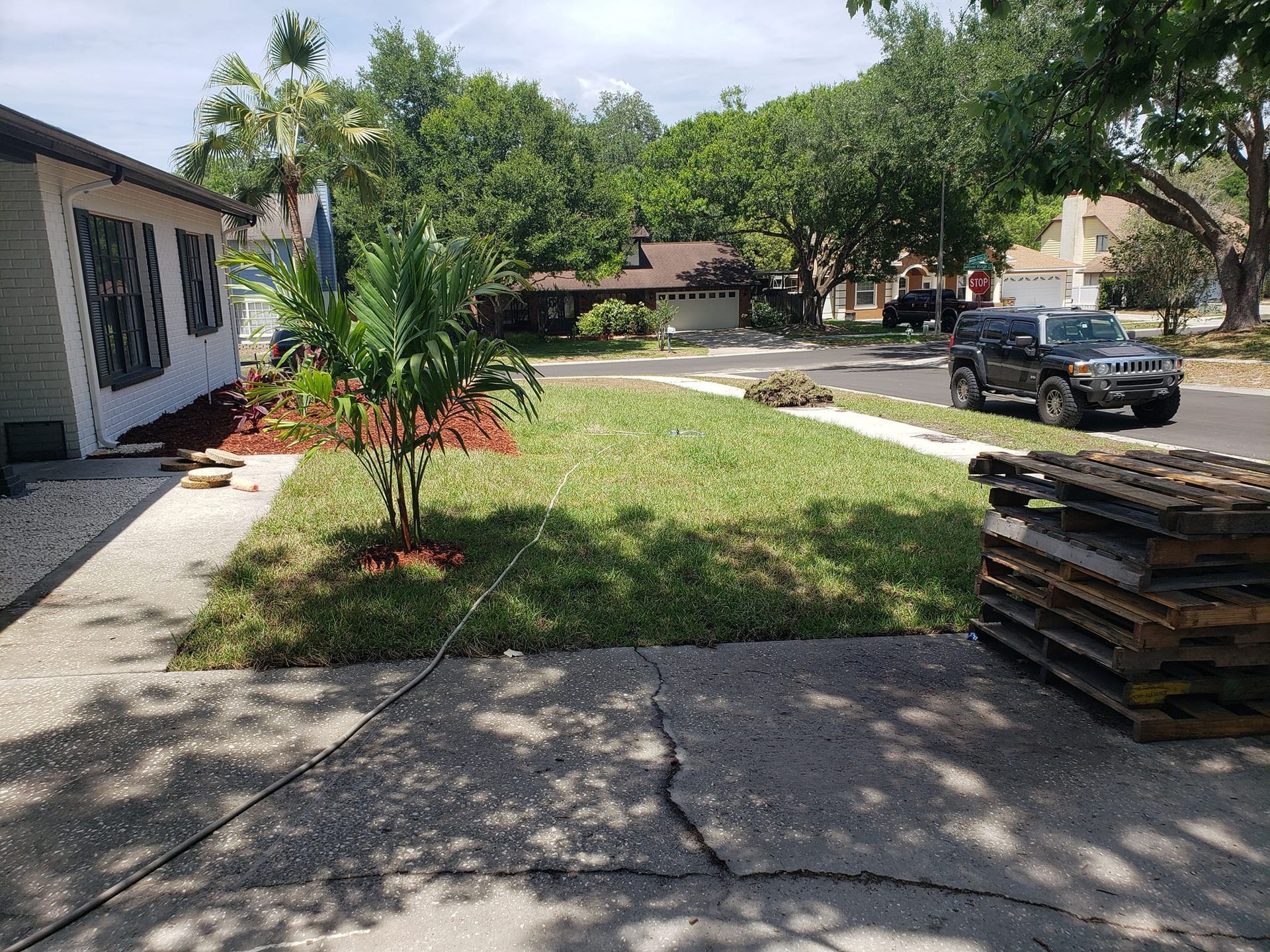 A car is parked in front of a house next to a stack of wooden pallets.