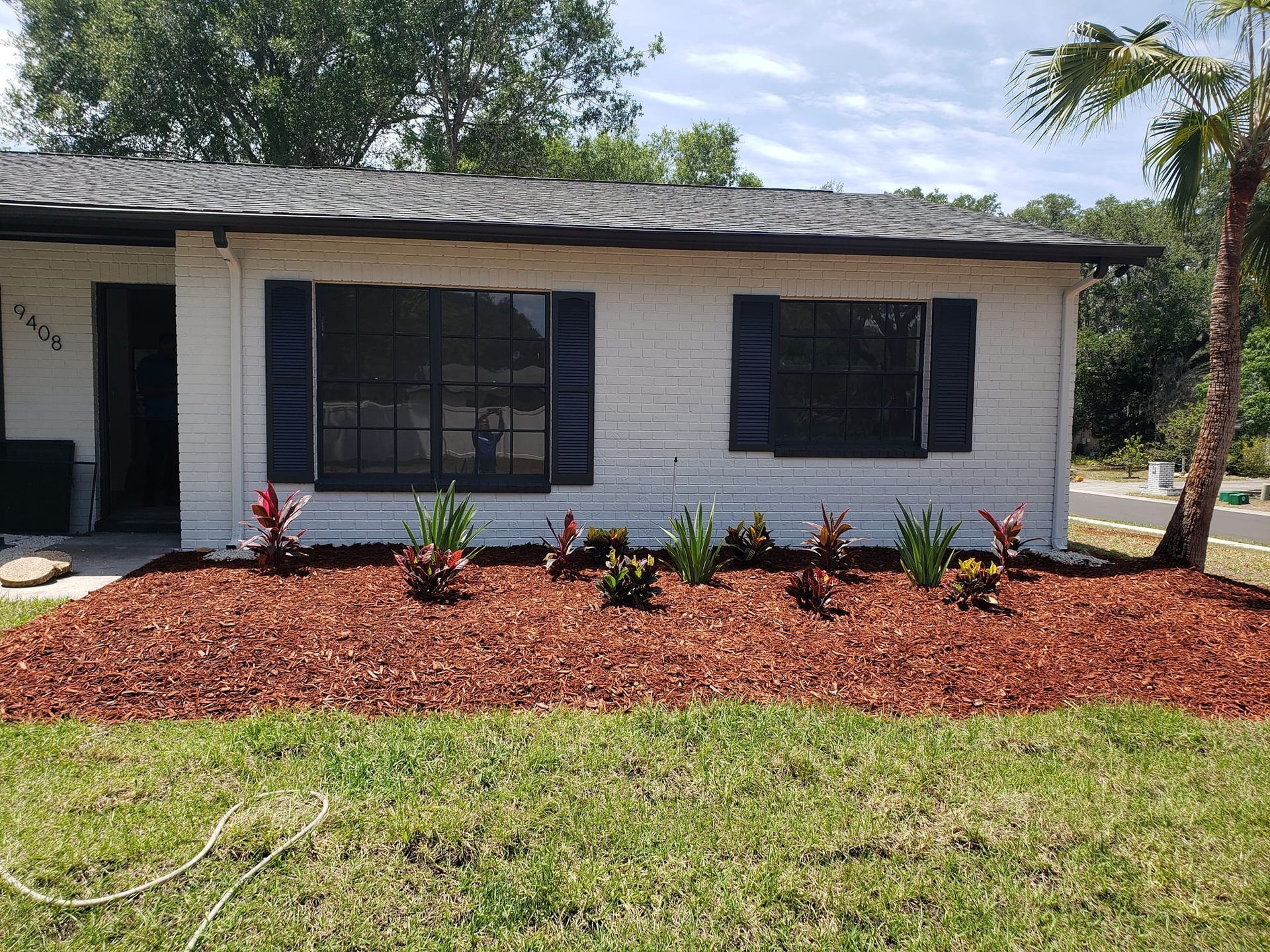A white house with blue shutters and mulch in front of it.