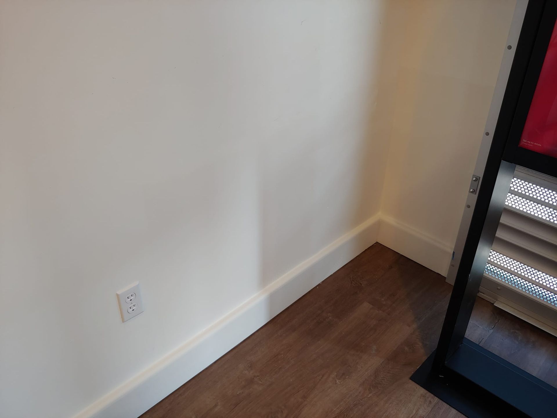 A corner of a room with a white wall and wood floor