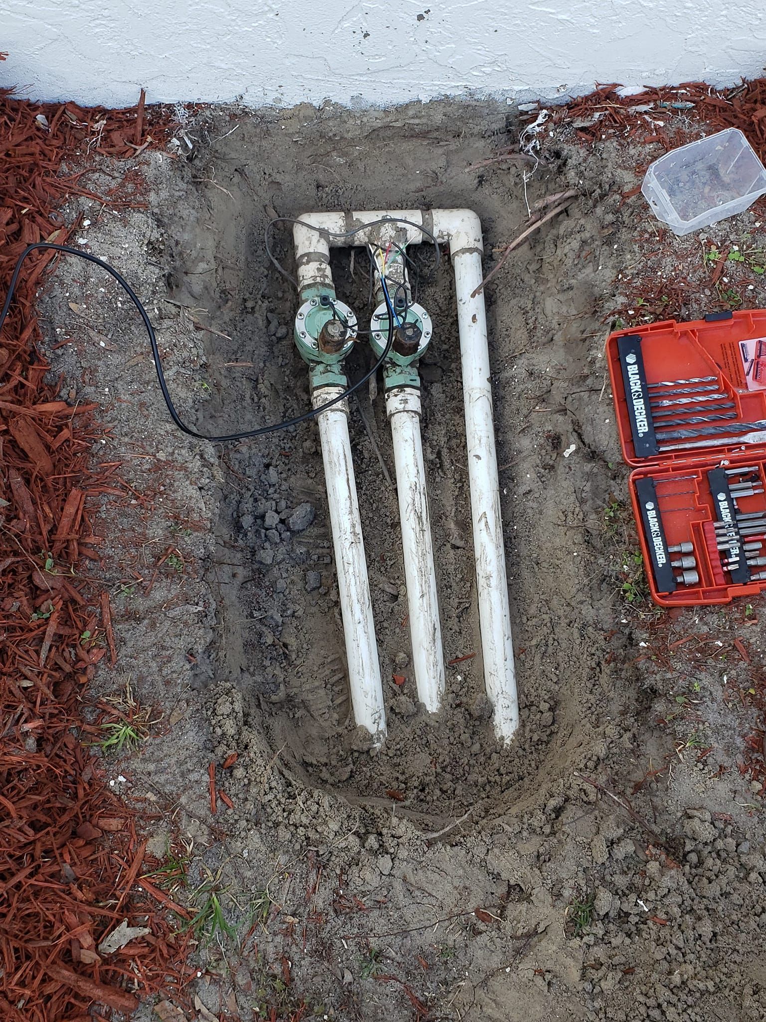 A water meter is sitting in the dirt next to a box of tools.