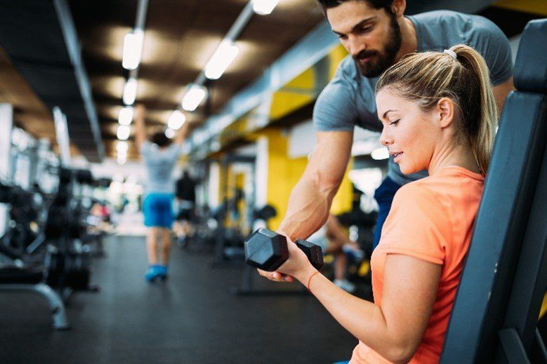 A girl trainee assisted to do private coaching on dumbells by professional Saxon coach