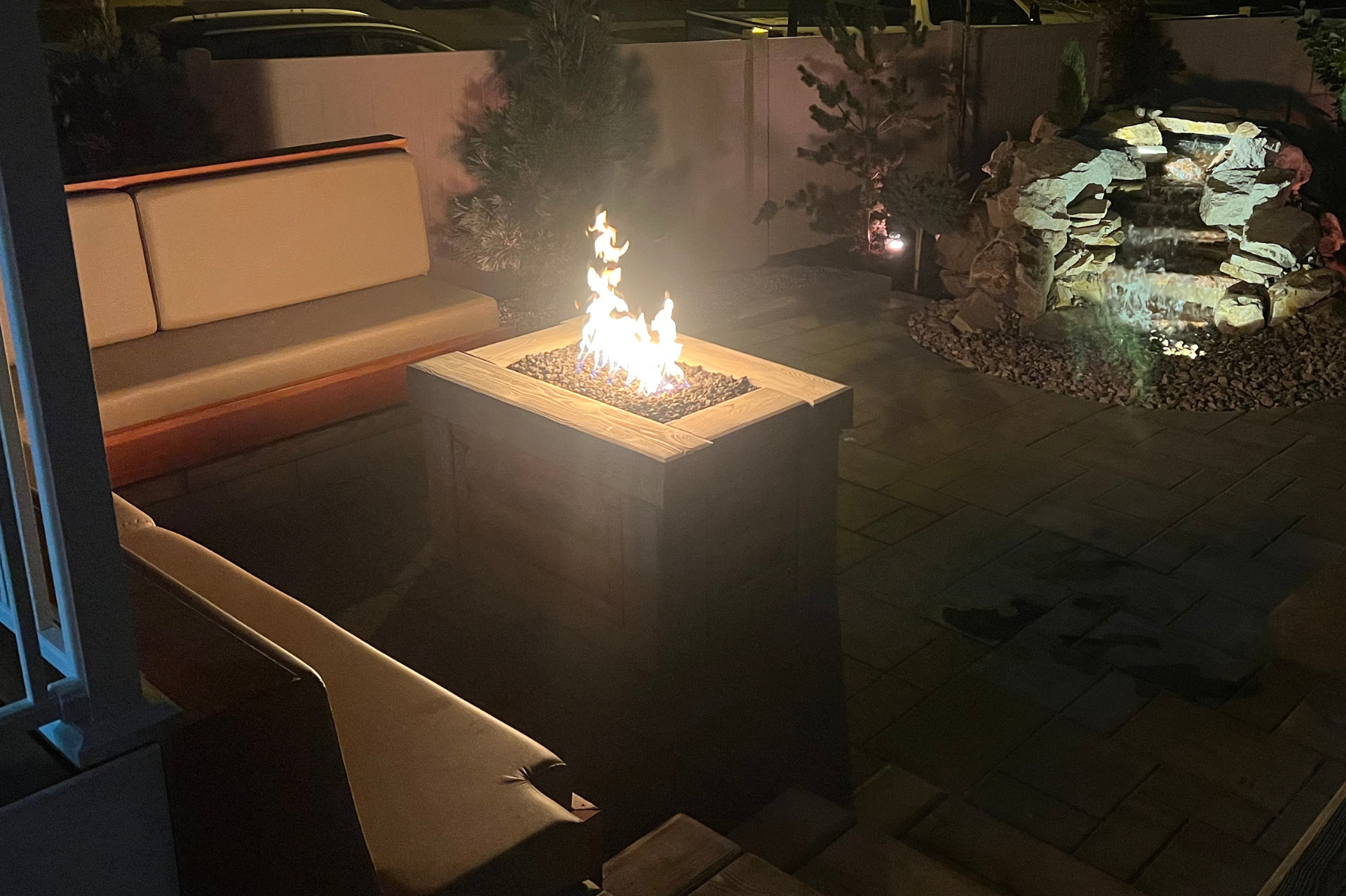 A fire pit is lit up in the middle of a patio at night.