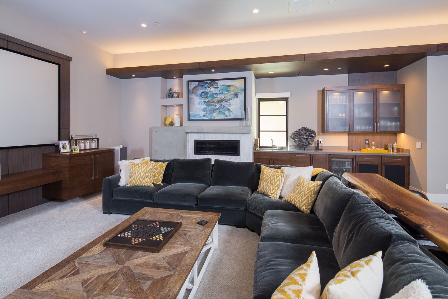 A living room with a large sectional couch and a projector screen.