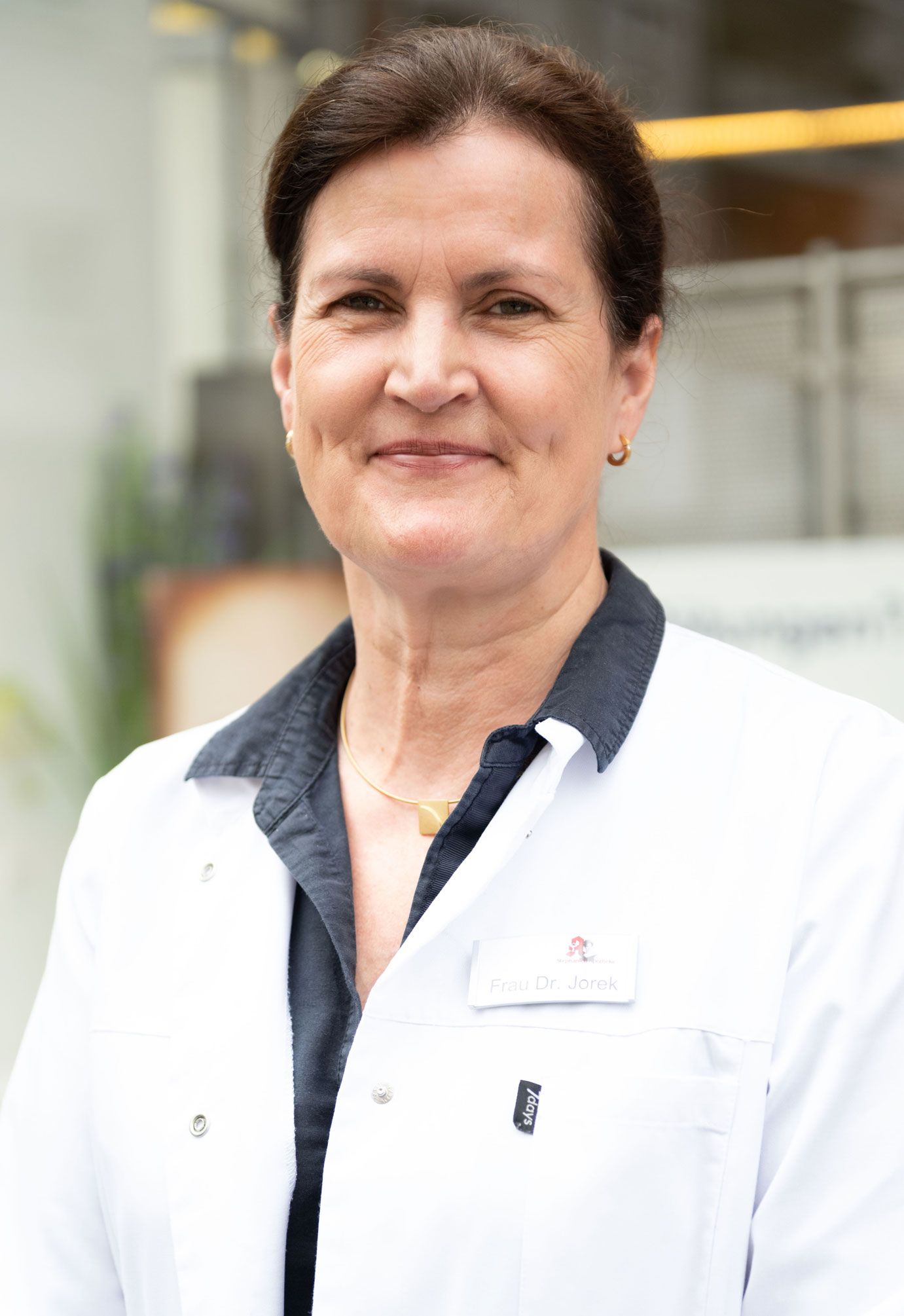 Eine Frau in einem weißen Laborkittel lächelt in die Kamera.