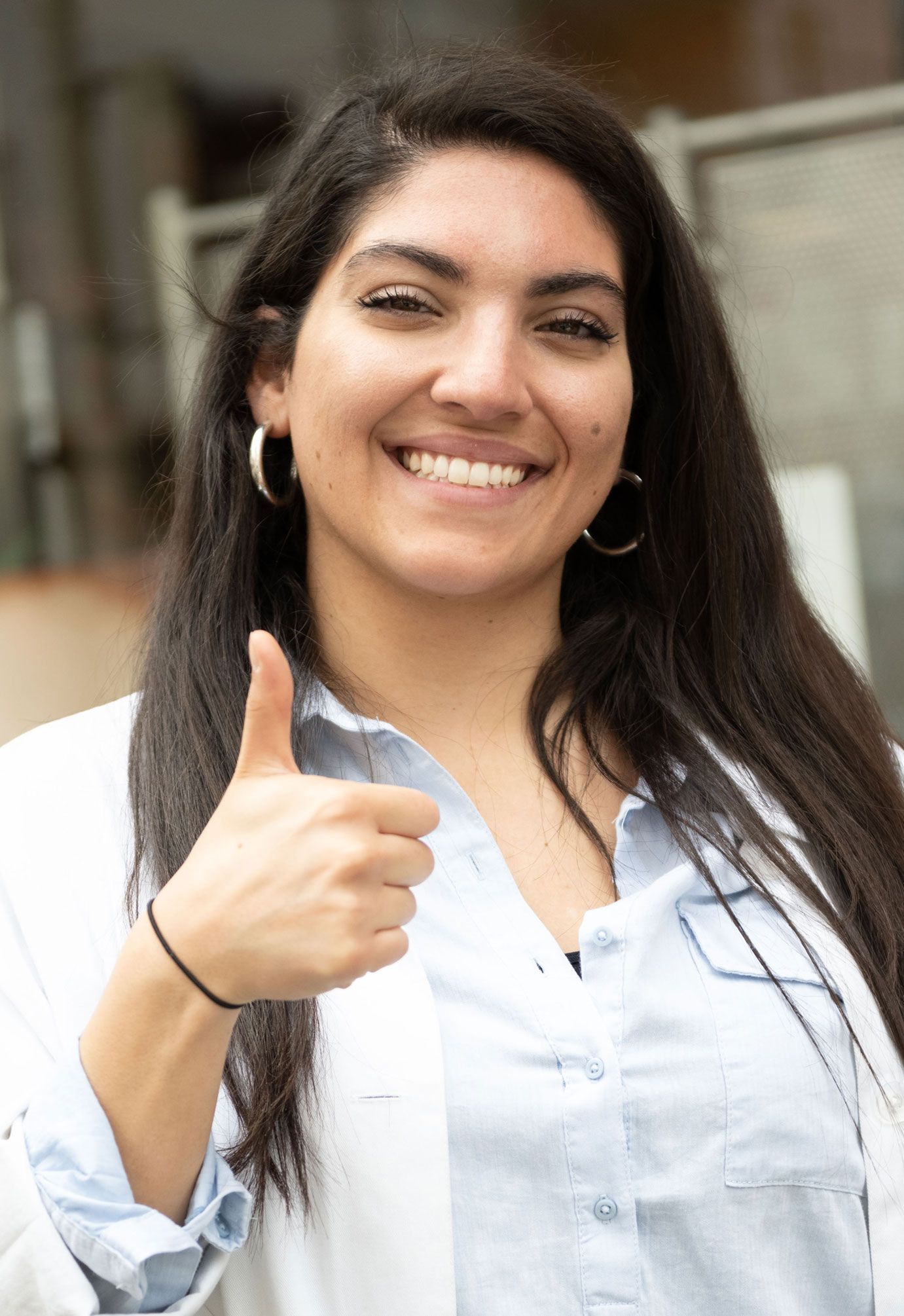 Eine Frau im weißen Kittel lächelt und zeigt mit dem Daumen nach oben.