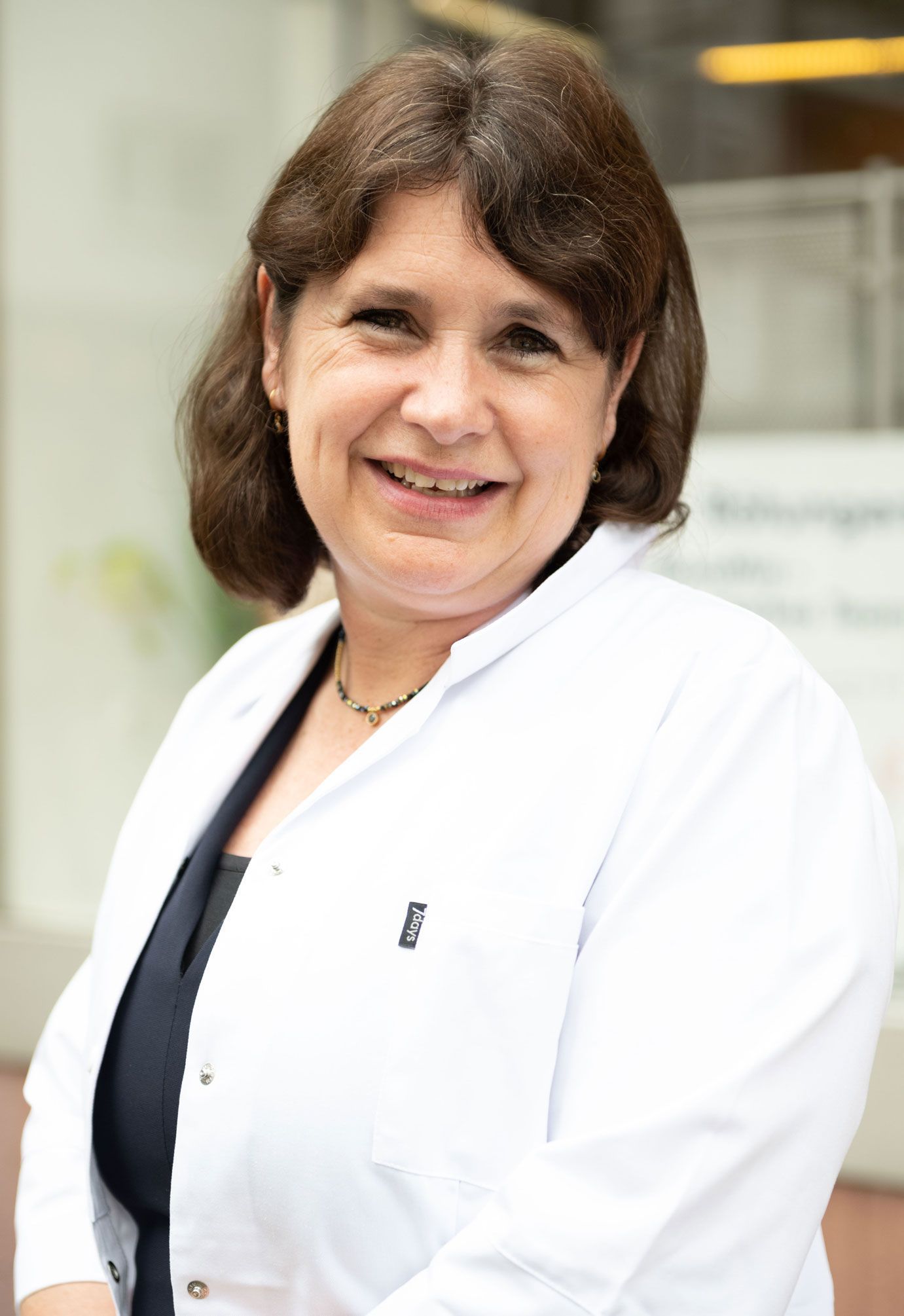 Eine Frau in einem weißen Laborkittel lächelt in die Kamera.