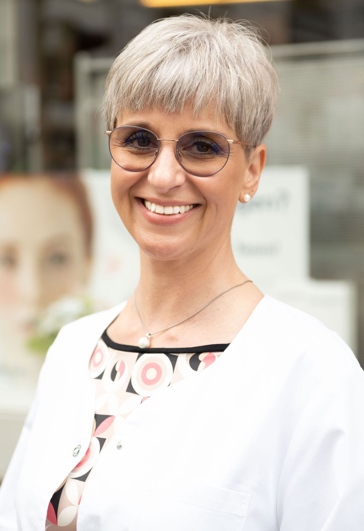Eine Frau mit Brille und weißem Kittel lächelt in die Kamera.