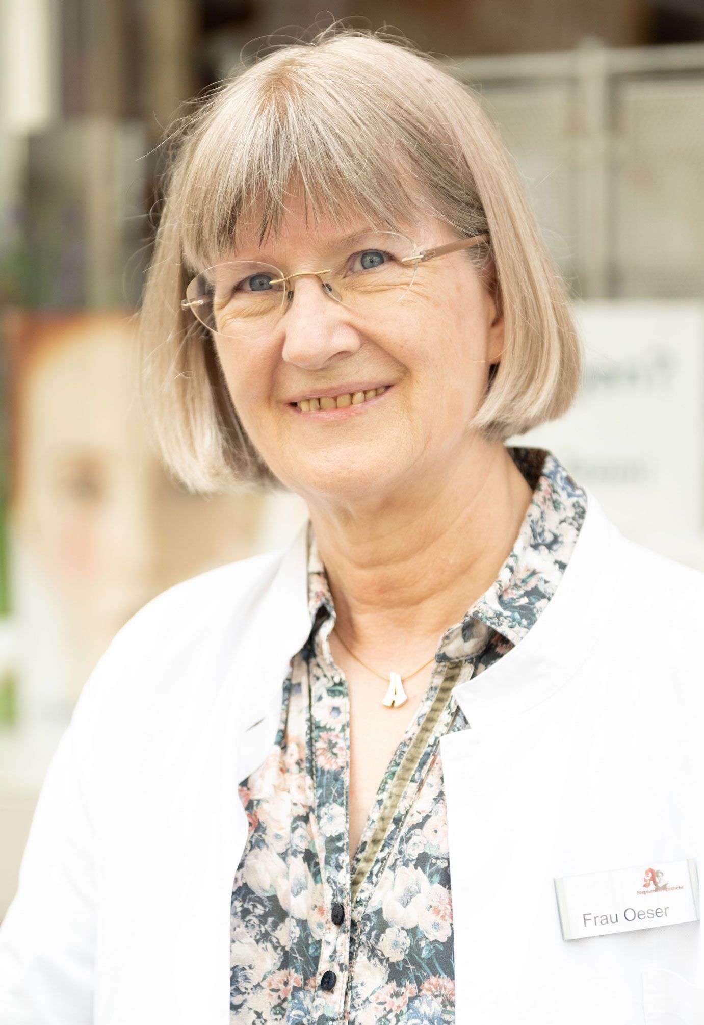 Eine Frau mit Brille und weißem Kittel lächelt in die Kamera.