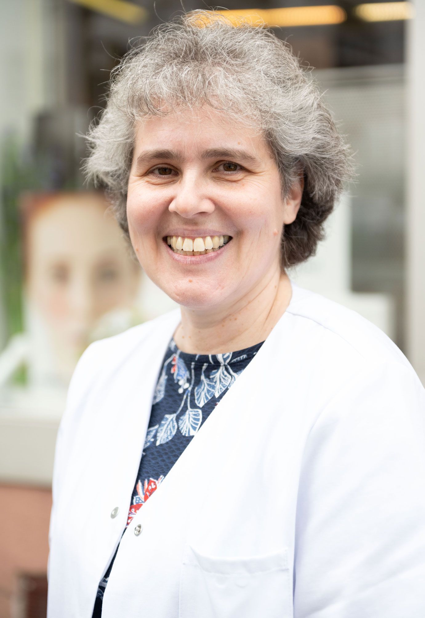 Eine Frau im weißen Laborkittel lächelt in die Kamera