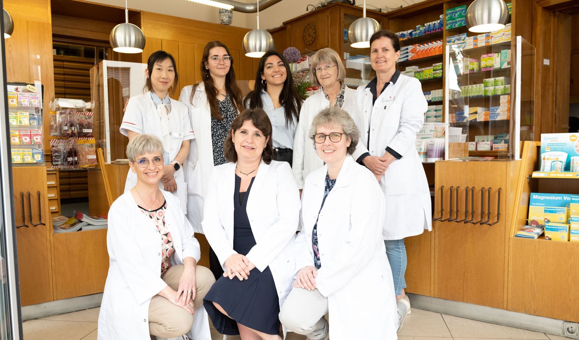 Eine Gruppe von Frauen in weißen Kitteln posiert in einer Apotheke für ein Foto.