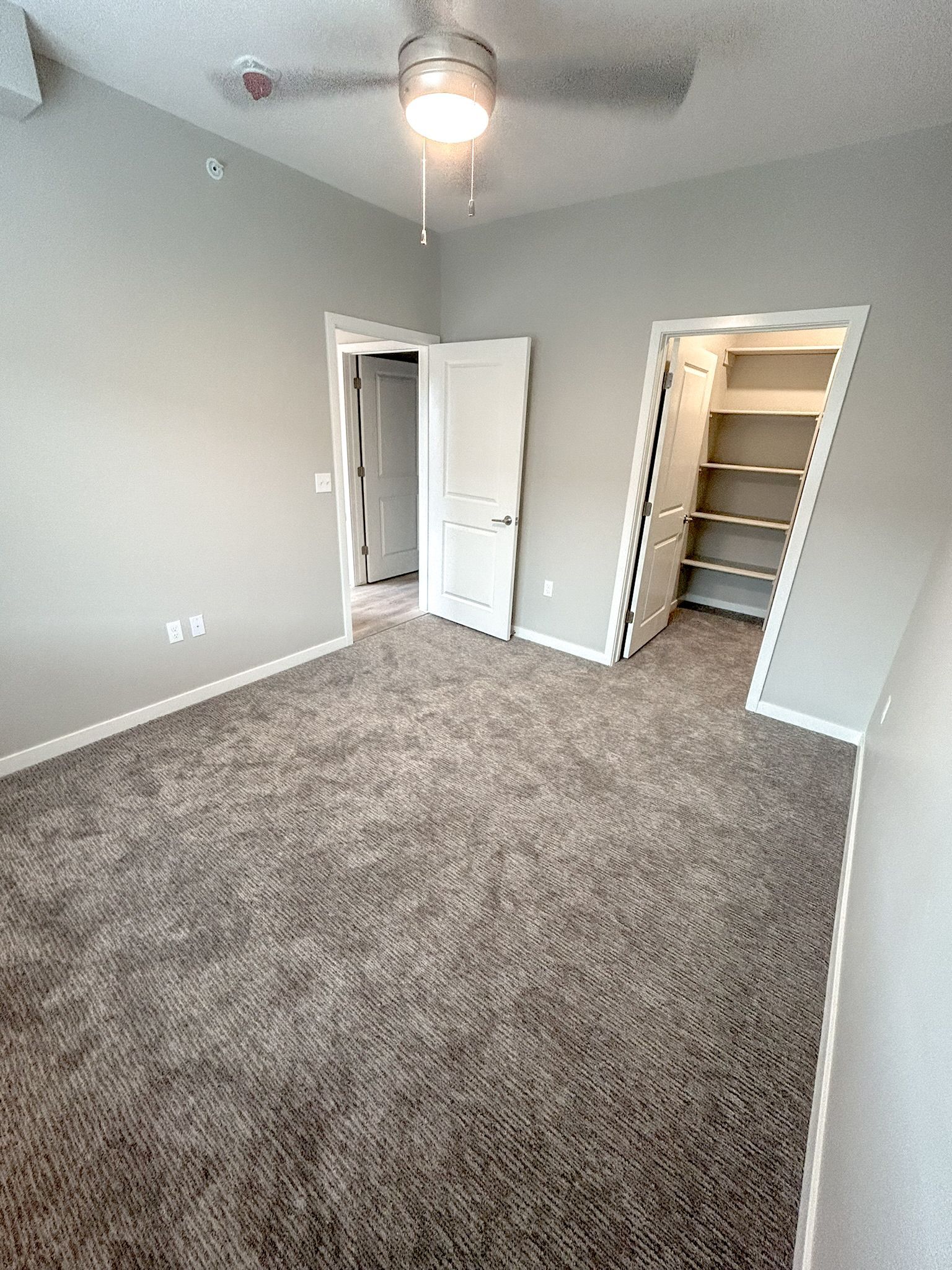 An empty bedroom with a ceiling fan and a walk in closet.