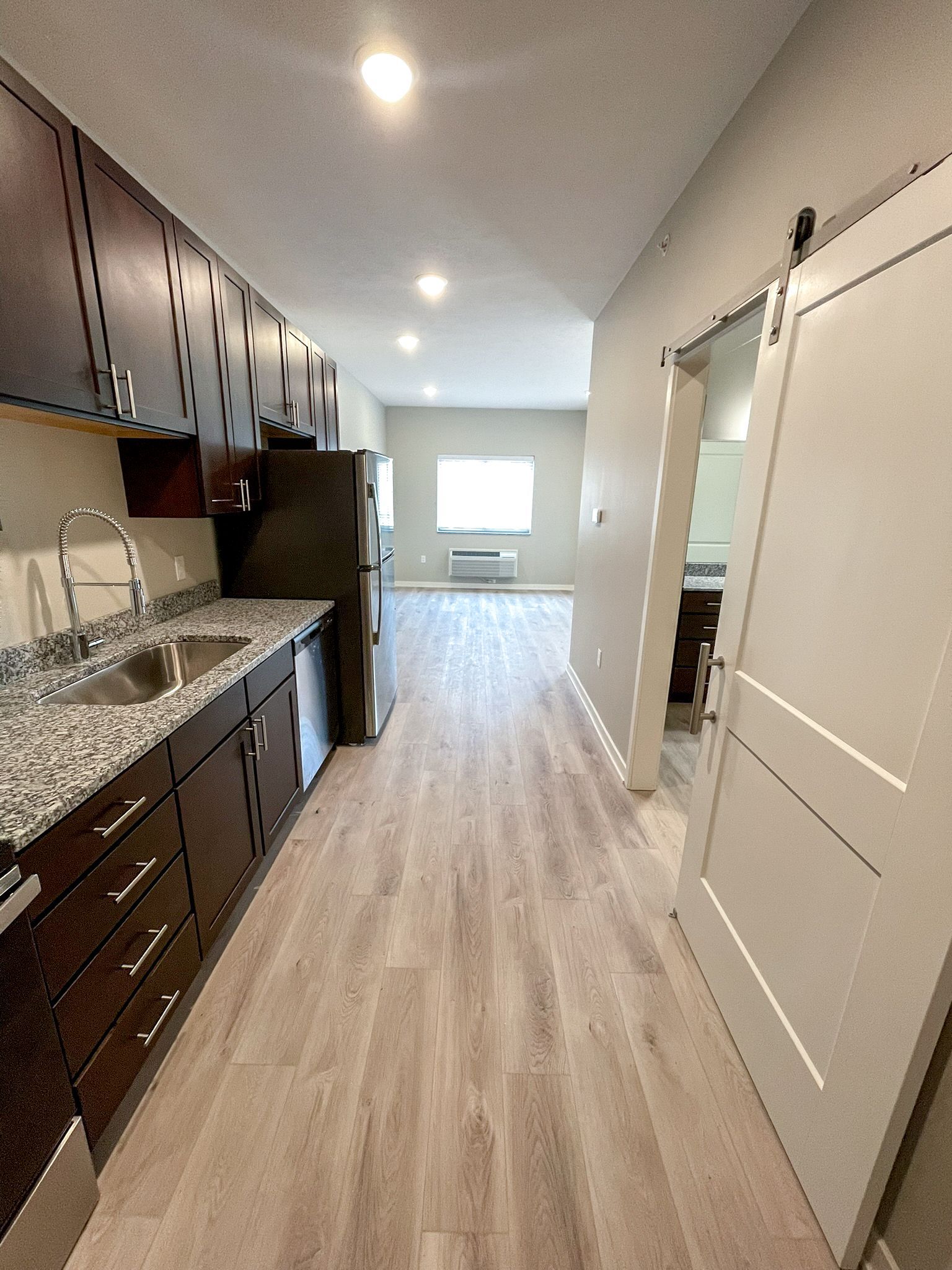 A long hallway leading to a kitchen with granite counter tops and stainless steel appliances.