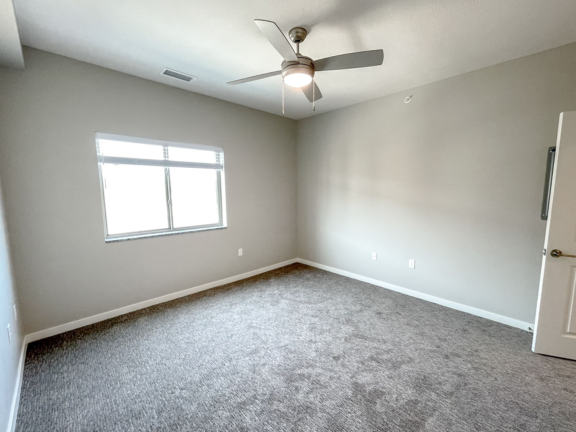 Empty bedroom with gray carpet, light walls, a window, and a ceiling fan.