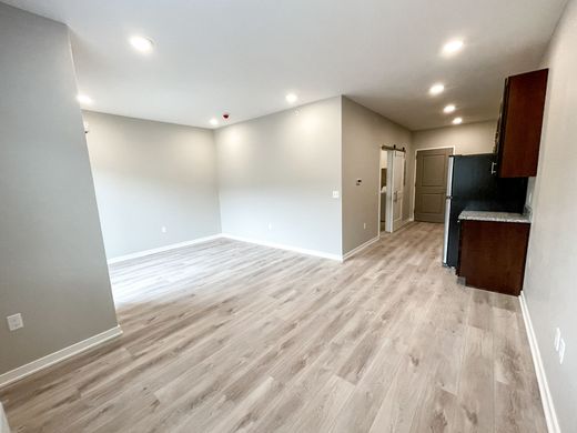 A living room with hardwood floors and a kitchen in the background.