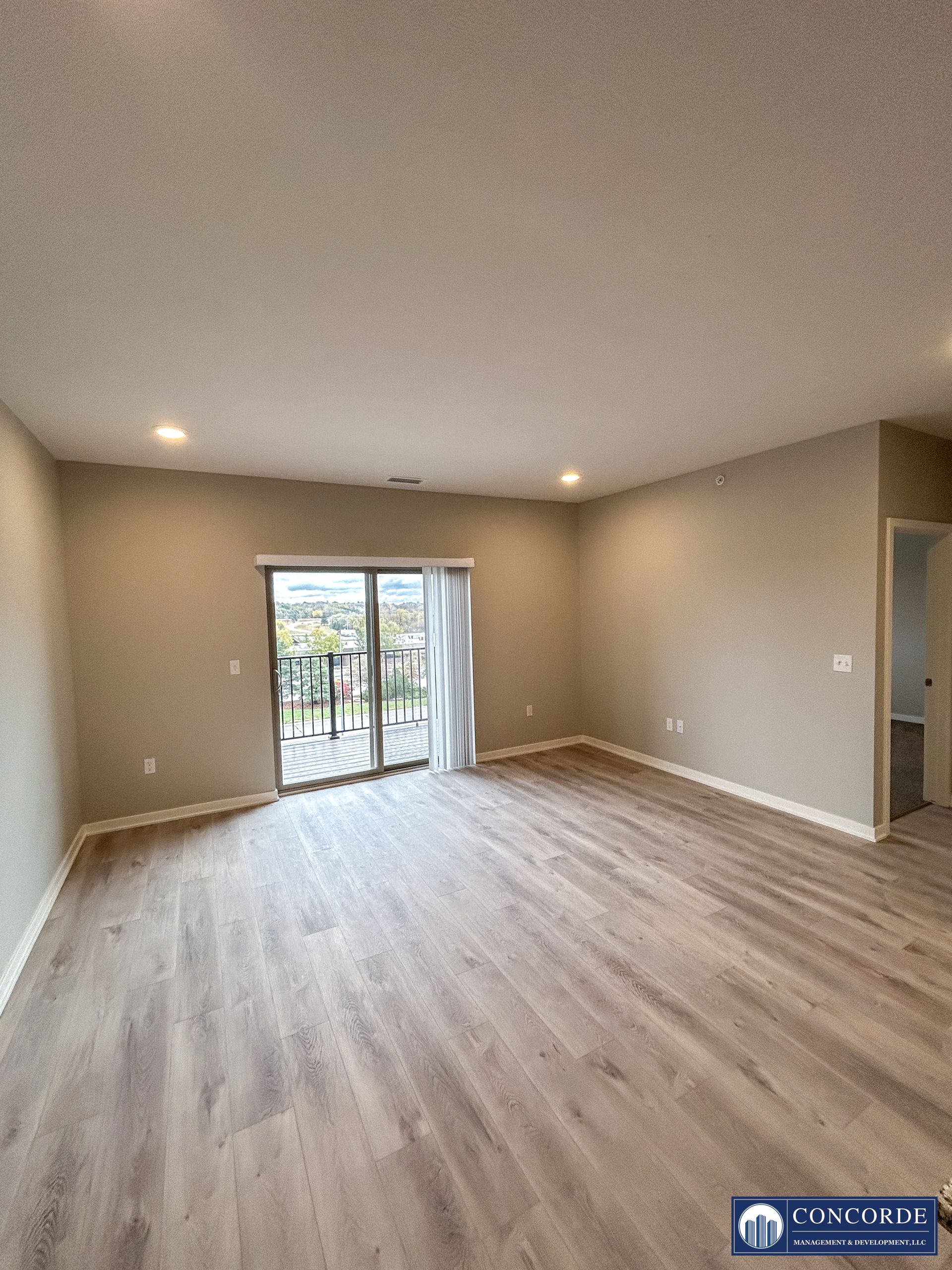 Empty beige living room with light wood floors and sliding glass doors to a patio.