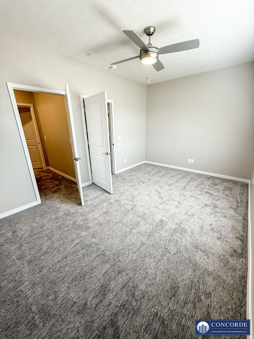 A bedroom with a ceiling fan and a gray carpet.