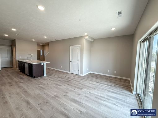 A large empty living room with hardwood floors and a kitchen.