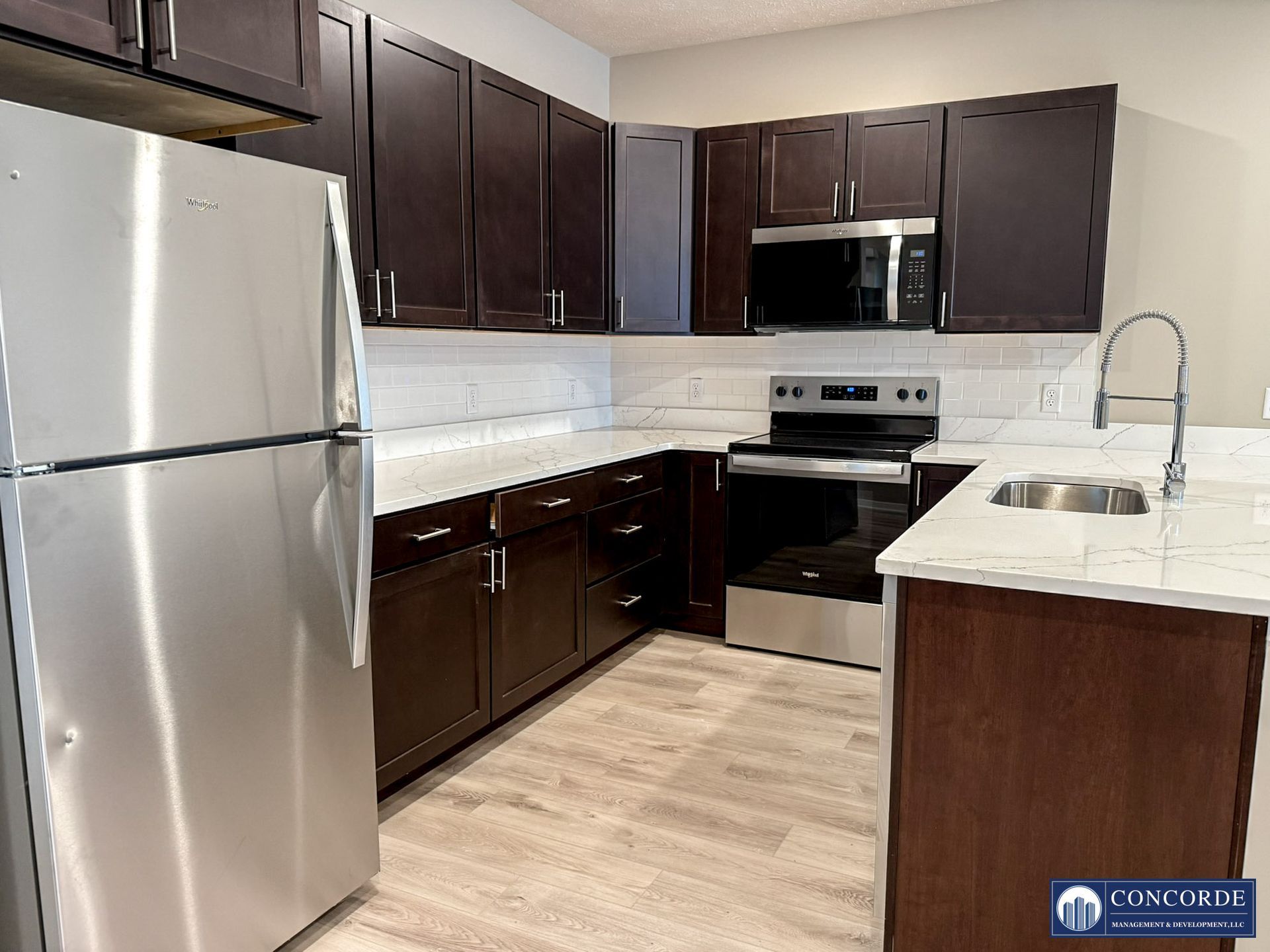 Modern kitchen with stainless steel appliances, dark cabinets, white countertops, and light wood flooring