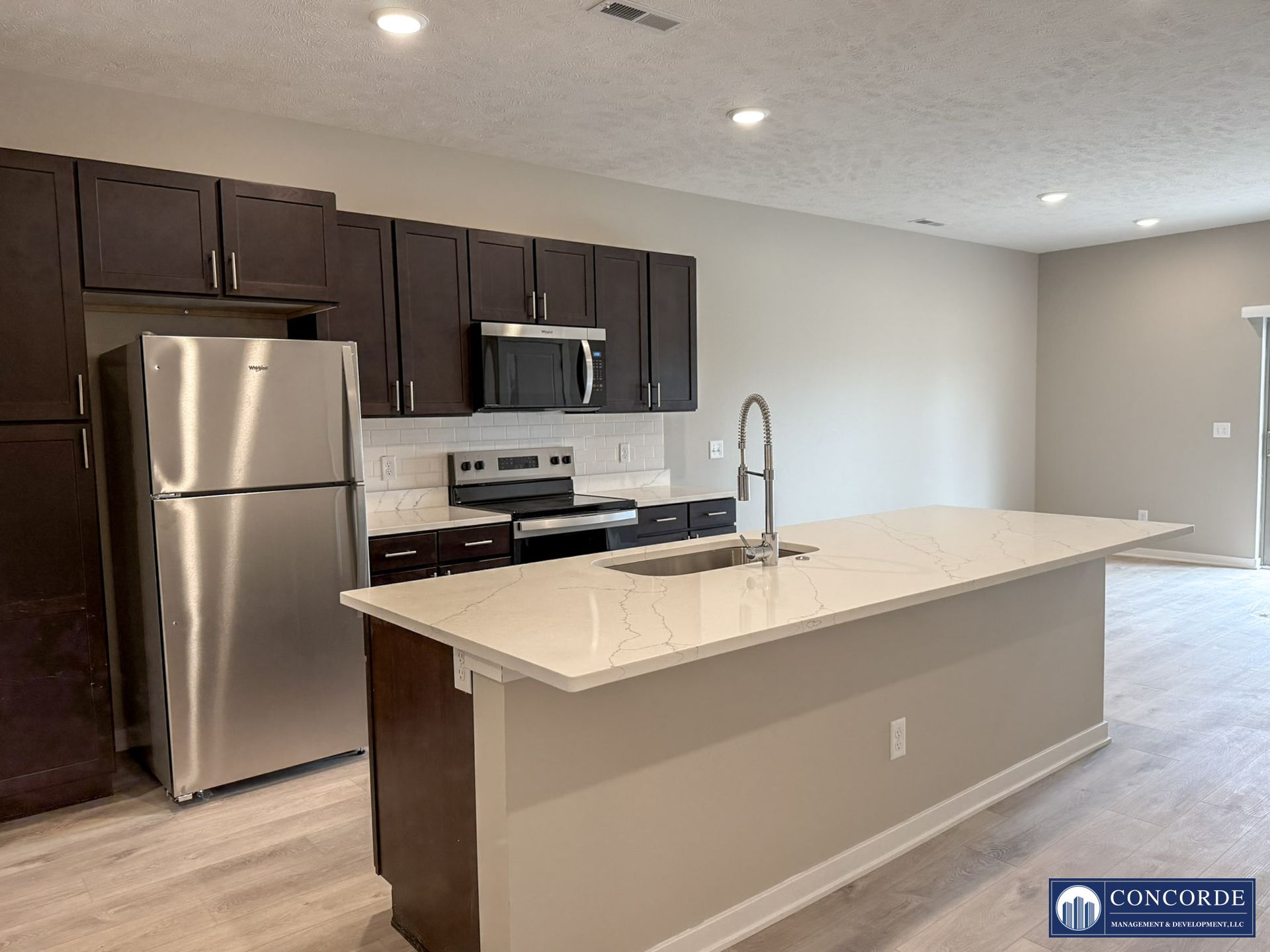 Modern kitchen with stainless steel appliances, dark cabinets, and a large light-colored island