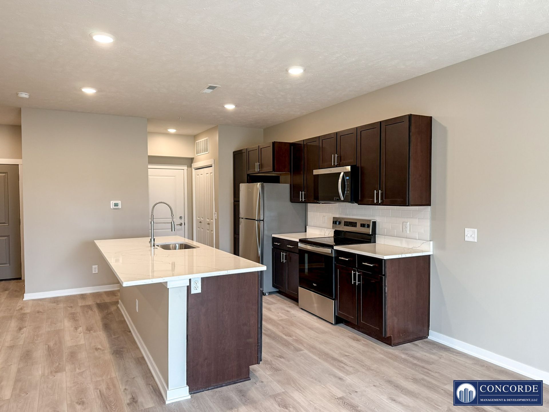 Modern kitchen with dark cabinets, stainless appliances, and a white island in an open room