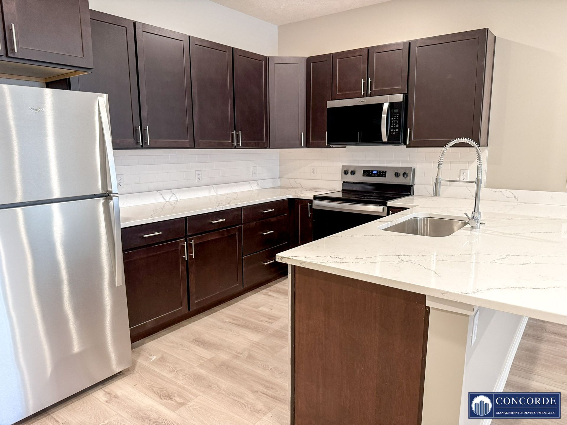 Modern kitchen with dark wood cabinets, stainless steel appliances, and a white marble island countertop