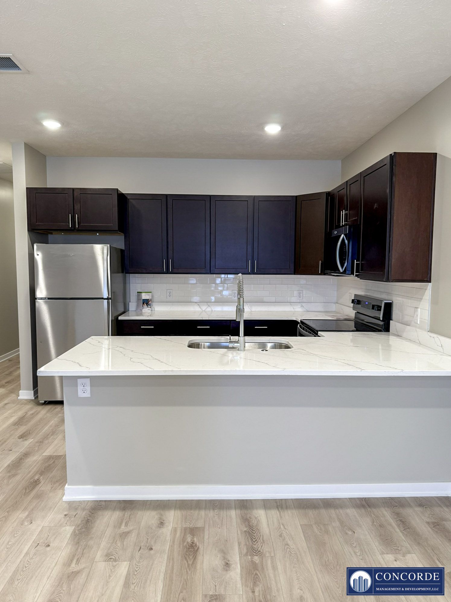 Modern kitchen with dark cabinets, stainless fridge, white island, and recessed lighting