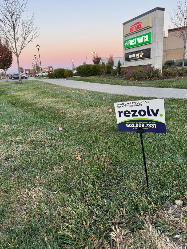A political sign is sitting in the grass in front of a building.