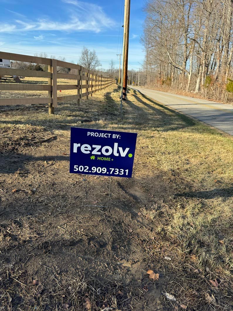 A for sale sign is sitting on the side of a dirt road next to a wooden fence.