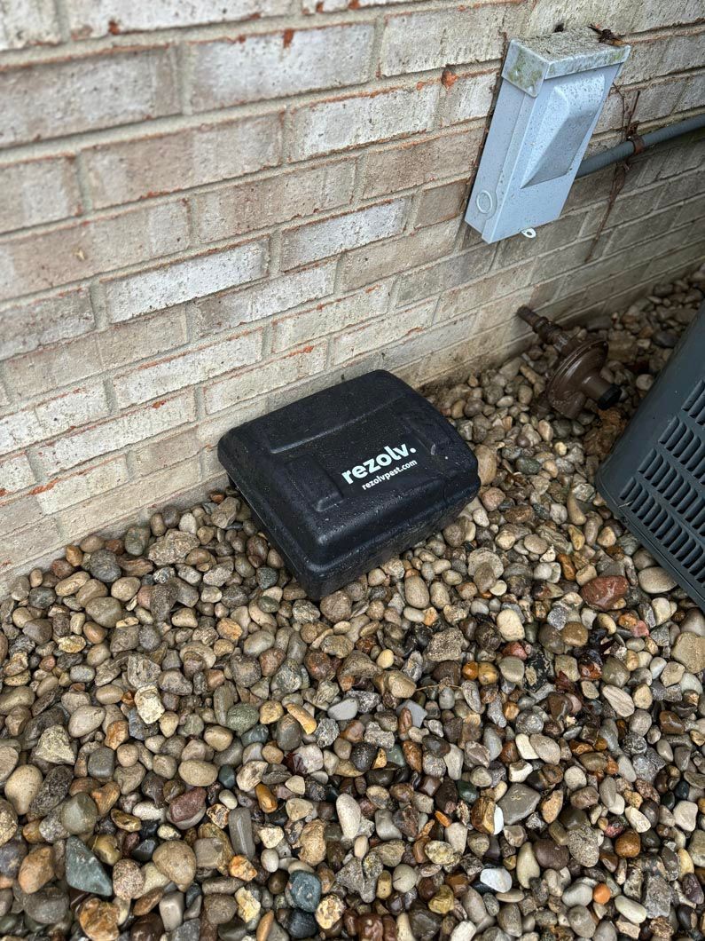 A black box is sitting on a pile of rocks next to a brick wall.