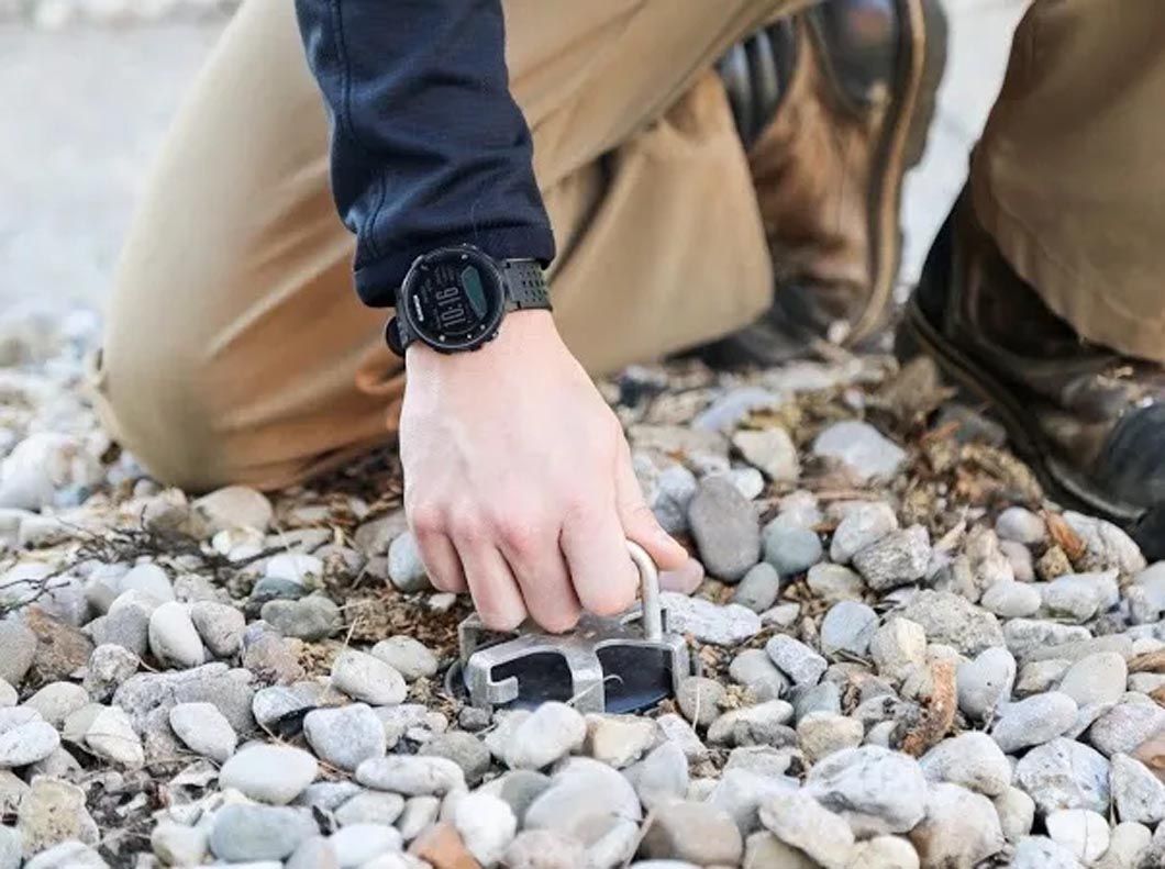 A person wearing a watch is kneeling on a pile of rocks.
