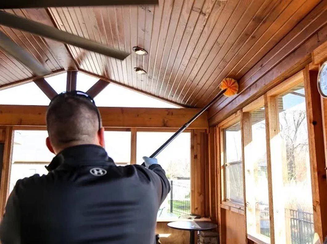A man is cleaning the ceiling of a room with a broom.
