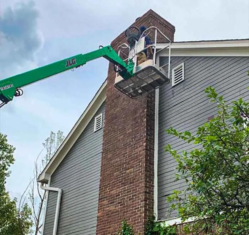 A man is cleaning a brick chimney on the side of a house.