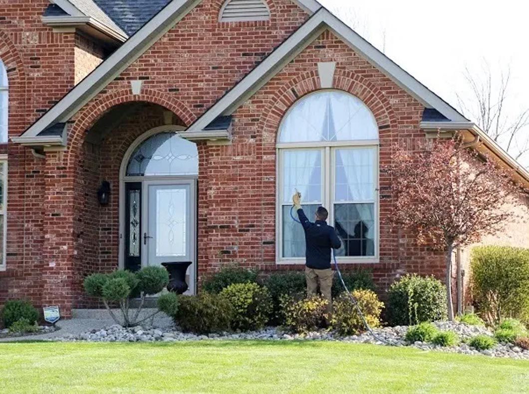 A man is cleaning the windows of a brick house.