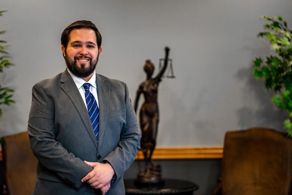 Brendan Burke posing in front of a small bronze statue of Lady Justice