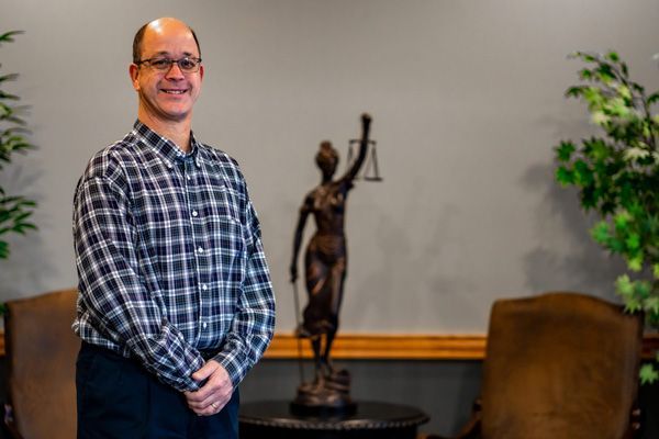 Robert Martin posing in front of a small bronze statue of Lady Justice