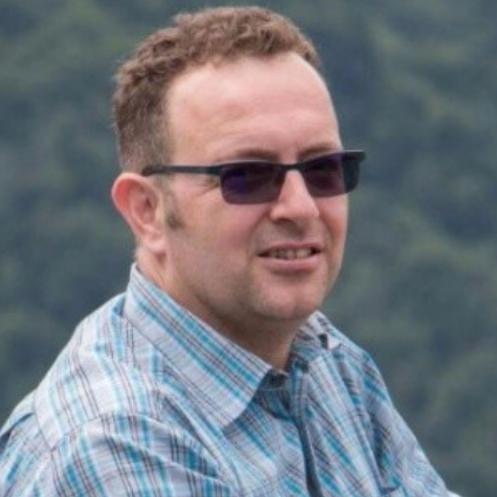 A man wearing sunglasses and a plaid shirt is smiling for the camera.