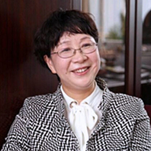 A woman wearing glasses and a black and white jacket is smiling.