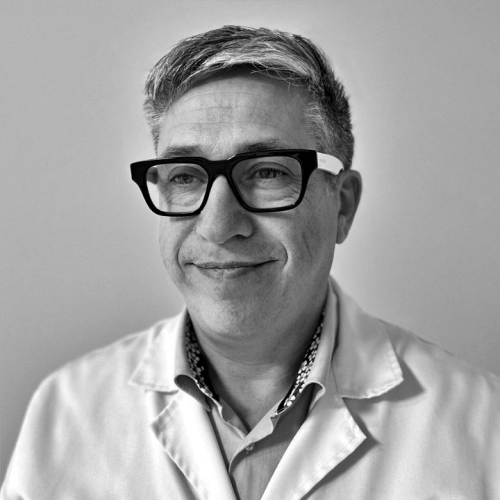 A black and white photo of a man wearing glasses and a lab coat.