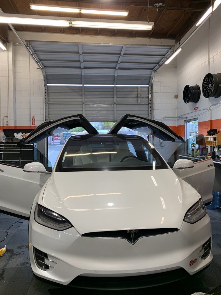 A white tesla model x is parked in a garage with its doors open.
