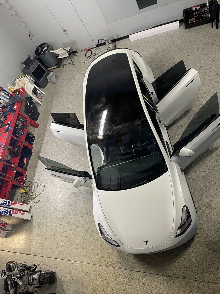 A white tesla model 3 is parked in a garage with its doors open.